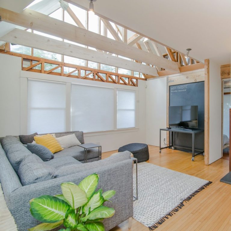 Modern living room with a grey sofa, wooden beams, and a large TV.