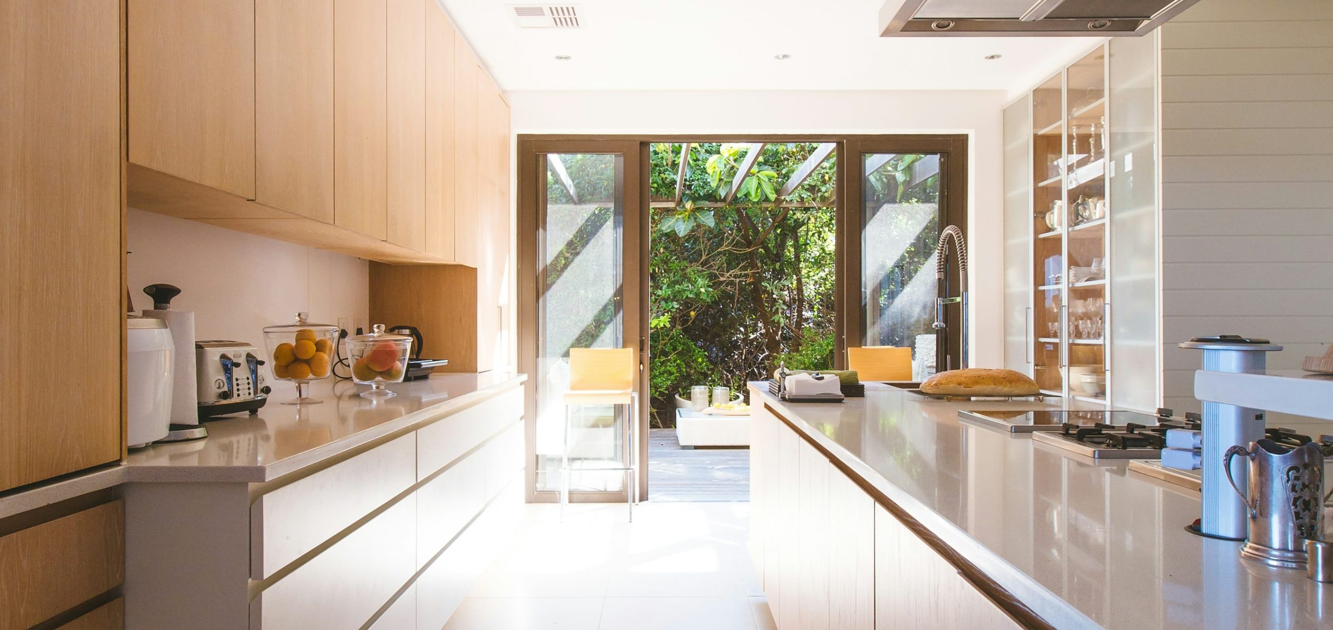 Modern kitchen with wooden cabinetry and a view of greenery through large glass doors.